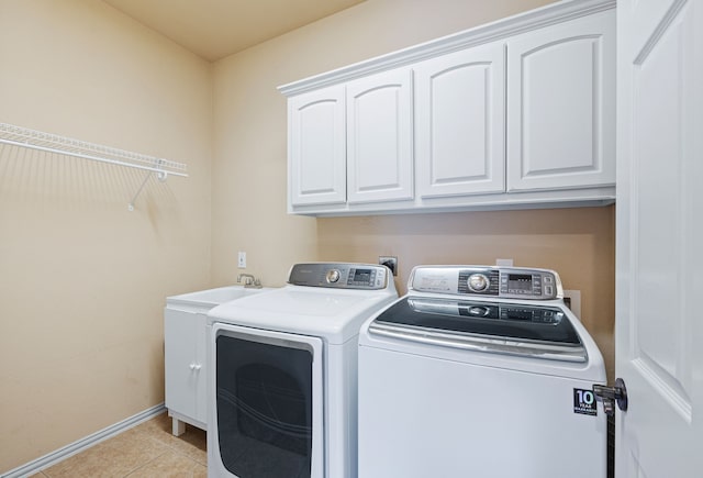 clothes washing area featuring cabinets, light tile patterned flooring, and washing machine and dryer