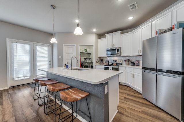 kitchen featuring appliances with stainless steel finishes, a kitchen island with sink, sink, pendant lighting, and white cabinets