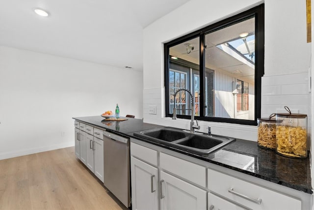 kitchen with white cabinetry, dishwasher, sink, light hardwood / wood-style flooring, and dark stone countertops