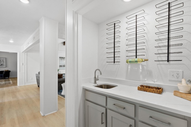 bar with gray cabinets, light stone countertops, sink, and light hardwood / wood-style flooring