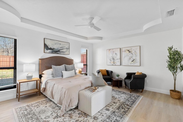 bedroom featuring multiple windows, light wood-type flooring, a raised ceiling, and ceiling fan