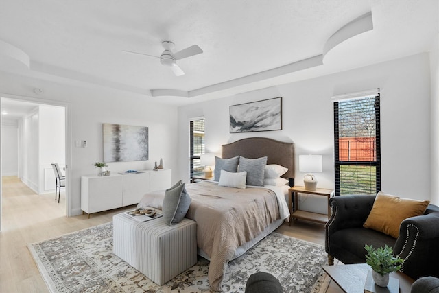 bedroom featuring light wood-type flooring, a raised ceiling, and ceiling fan