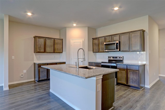 kitchen featuring sink, decorative backsplash, an island with sink, light stone counters, and stainless steel appliances