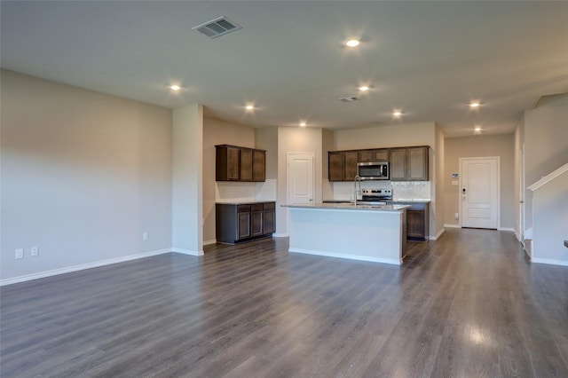 kitchen with sink, appliances with stainless steel finishes, dark hardwood / wood-style flooring, a kitchen island with sink, and backsplash