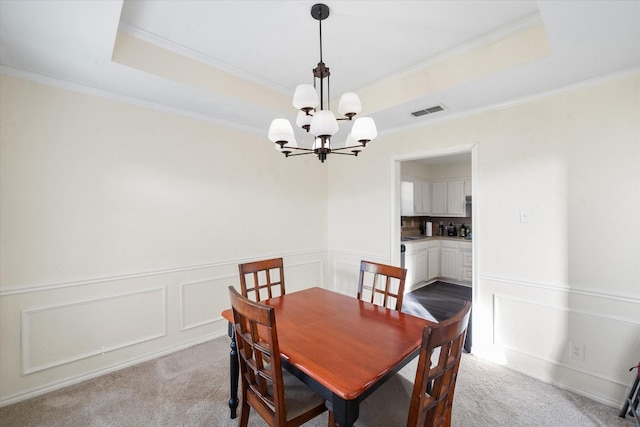 carpeted dining space with a tray ceiling, crown molding, and a notable chandelier