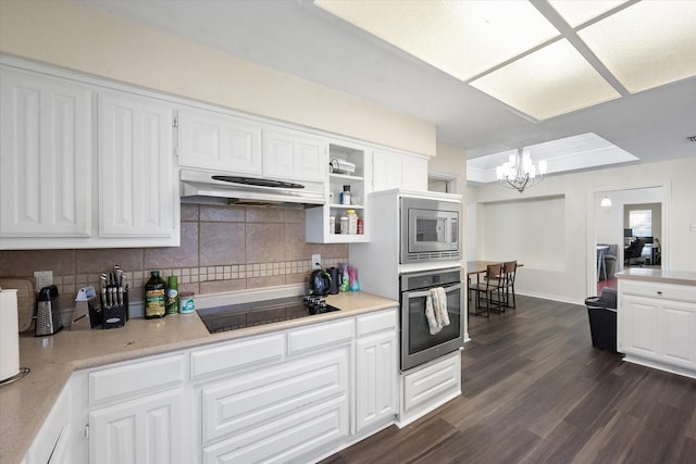 kitchen featuring dark wood-type flooring, white cabinets, decorative backsplash, appliances with stainless steel finishes, and a chandelier