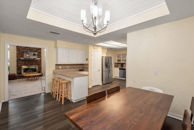 dining area featuring an inviting chandelier, a tray ceiling, a fireplace, and dark hardwood / wood-style floors