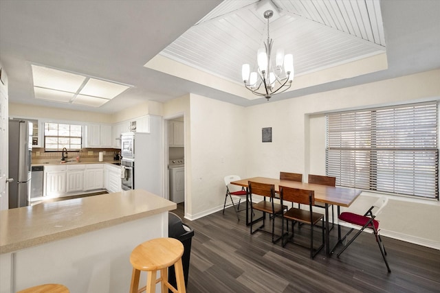 kitchen featuring hanging light fixtures, appliances with stainless steel finishes, dark hardwood / wood-style flooring, white cabinetry, and washer / clothes dryer