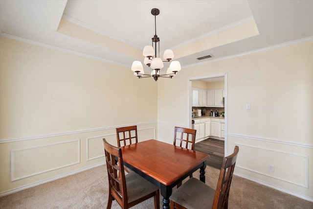 dining room featuring dark carpet, a tray ceiling, crown molding, and a chandelier