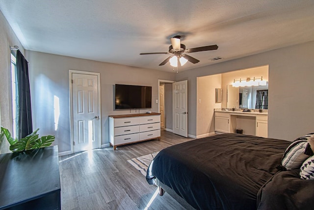 bedroom featuring a textured ceiling, ensuite bathroom, light hardwood / wood-style flooring, and ceiling fan