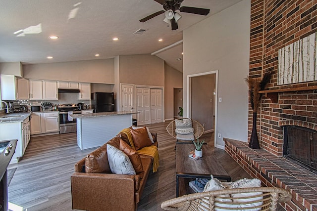 living room with ceiling fan, sink, high vaulted ceiling, a fireplace, and hardwood / wood-style flooring