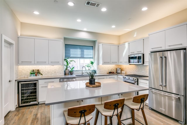 kitchen with a breakfast bar, a center island, white cabinets, stainless steel appliances, and beverage cooler