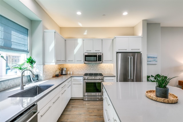 kitchen featuring decorative backsplash, sink, high quality appliances, white cabinets, and light hardwood / wood-style floors