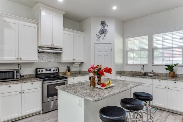 kitchen with light stone counters, stainless steel appliances, sink, white cabinets, and a center island