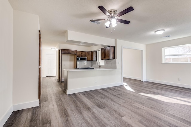 kitchen featuring dark brown cabinetry, sink, kitchen peninsula, light hardwood / wood-style floors, and a textured ceiling