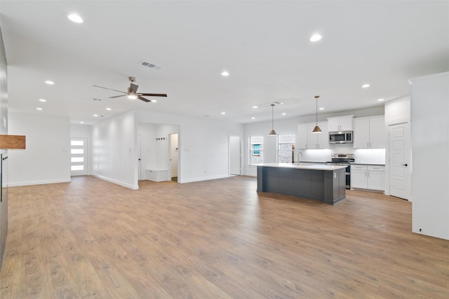 kitchen featuring appliances with stainless steel finishes, ceiling fan, white cabinets, hanging light fixtures, and an island with sink