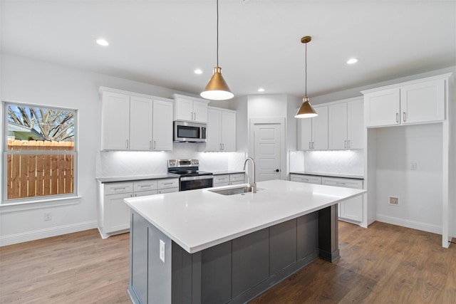 kitchen with white cabinetry, tasteful backsplash, pendant lighting, a center island with sink, and appliances with stainless steel finishes