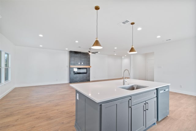 kitchen with gray cabinetry, sink, stainless steel dishwasher, an island with sink, and decorative light fixtures