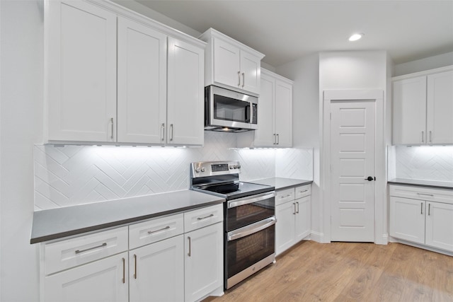 kitchen with decorative backsplash, white cabinets, light wood-type flooring, and appliances with stainless steel finishes