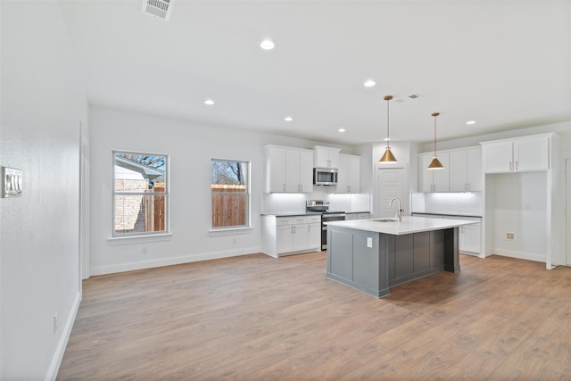 kitchen featuring sink, hanging light fixtures, a center island with sink, white cabinets, and appliances with stainless steel finishes