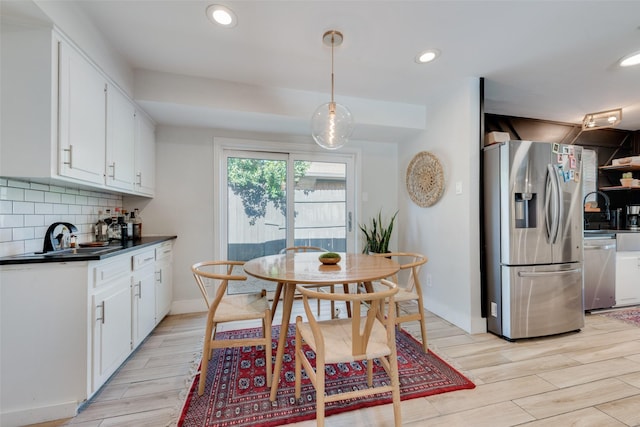 kitchen with hanging light fixtures, light hardwood / wood-style flooring, white cabinets, stainless steel appliances, and backsplash