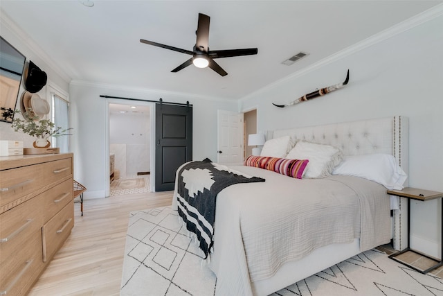 bedroom with crown molding, ceiling fan, ensuite bathroom, a barn door, and light wood-type flooring