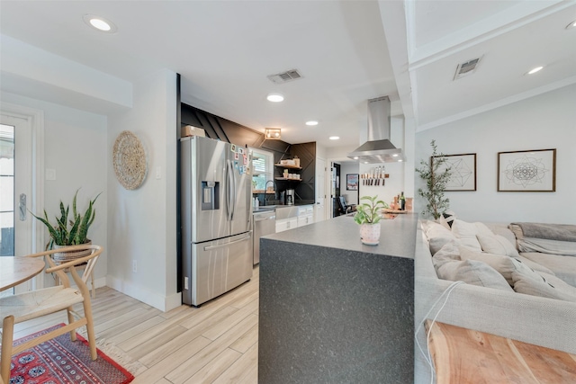 kitchen with wall chimney range hood, light wood-type flooring, kitchen peninsula, and appliances with stainless steel finishes