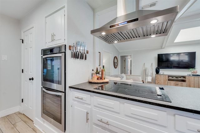 kitchen featuring double oven, lofted ceiling, white cabinets, island exhaust hood, and black electric cooktop