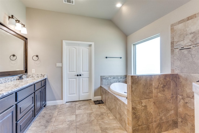 bathroom with tile patterned flooring, vanity, a relaxing tiled tub, and lofted ceiling