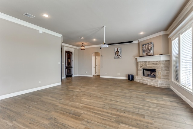 unfurnished living room featuring a stone fireplace, crown molding, and light wood-type flooring