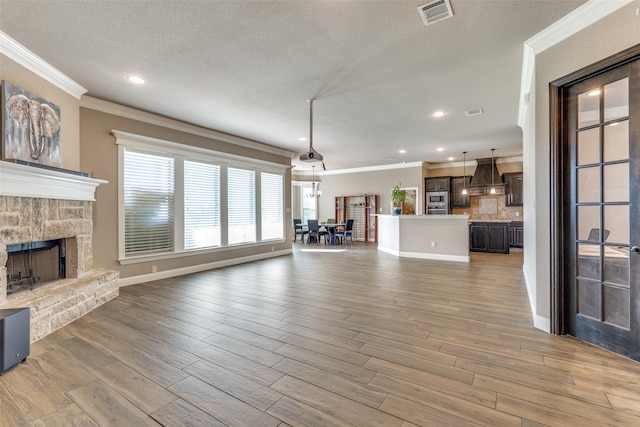 unfurnished living room featuring a stone fireplace, crown molding, and a textured ceiling