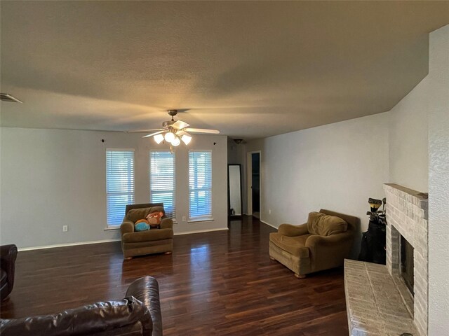 living room with ceiling fan, a fireplace, dark hardwood / wood-style flooring, and a textured ceiling