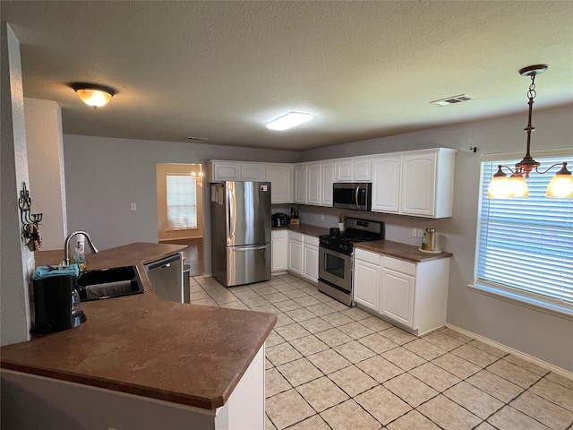 kitchen with sink, hanging light fixtures, light tile patterned floors, white cabinets, and appliances with stainless steel finishes