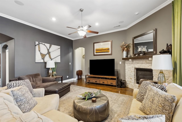 living room featuring ceiling fan, hardwood / wood-style floors, crown molding, and a stone fireplace