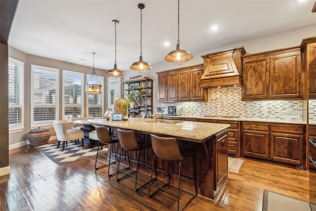 kitchen with decorative light fixtures, wood-type flooring, a breakfast bar area, and a center island with sink