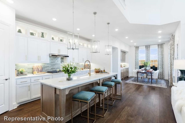 kitchen with backsplash, a center island with sink, hanging light fixtures, dark hardwood / wood-style floors, and white cabinetry