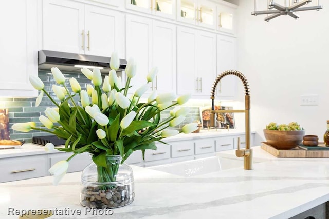 room details featuring decorative backsplash, light stone counters, sink, and white cabinets