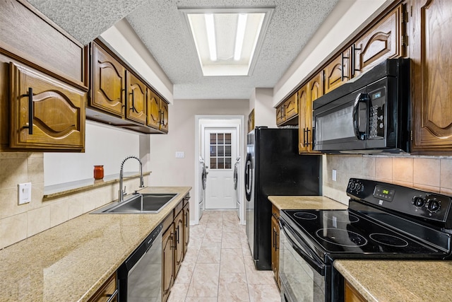 kitchen featuring black appliances, sink, decorative backsplash, light stone countertops, and independent washer and dryer