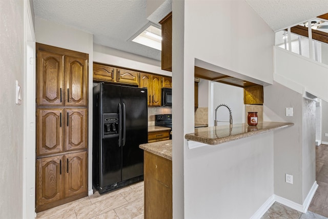 kitchen featuring kitchen peninsula, light stone countertops, black appliances, and a textured ceiling