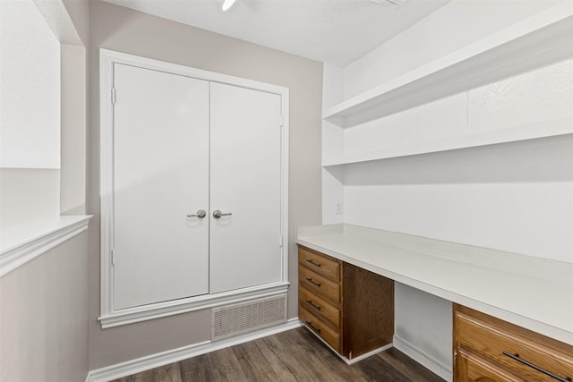 unfurnished office featuring a textured ceiling, built in desk, and dark hardwood / wood-style floors