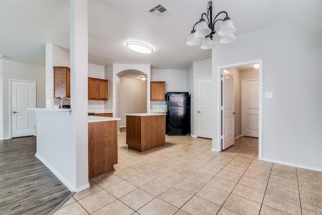 kitchen with a notable chandelier, kitchen peninsula, decorative light fixtures, black refrigerator, and light tile patterned flooring