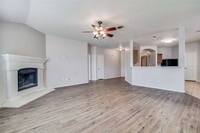 unfurnished living room with a tile fireplace, vaulted ceiling, light hardwood / wood-style flooring, and ceiling fan