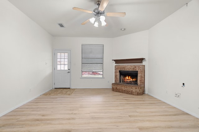 unfurnished living room with ceiling fan, a brick fireplace, and light wood-type flooring