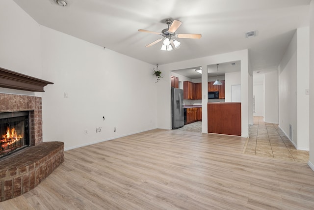 living room with a brick fireplace, ceiling fan, and light hardwood / wood-style flooring