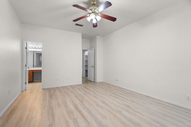 unfurnished bedroom with ensuite bath, a spacious closet, ceiling fan, and light wood-type flooring