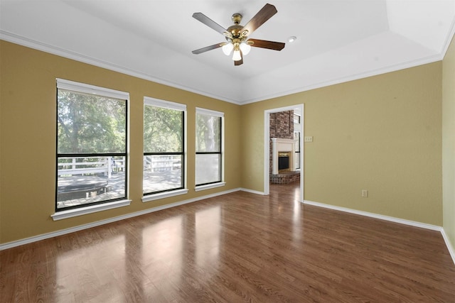 unfurnished room featuring a fireplace, dark hardwood / wood-style flooring, a raised ceiling, and ceiling fan