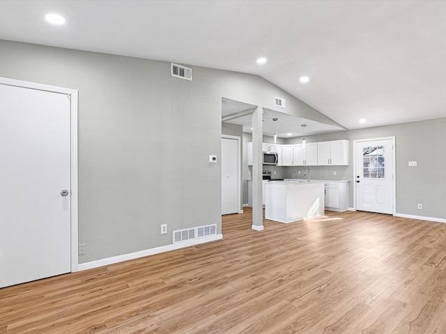 unfurnished living room with sink, light hardwood / wood-style floors, and lofted ceiling