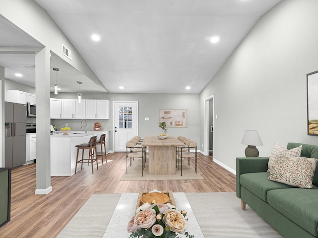 living room with light wood-type flooring, lofted ceiling, and sink