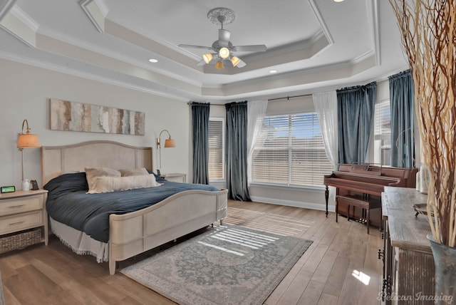 bedroom with crown molding, light hardwood / wood-style flooring, ceiling fan, and a tray ceiling