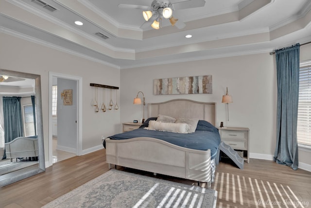 bedroom featuring ensuite bath, light wood-type flooring, ornamental molding, a tray ceiling, and ceiling fan